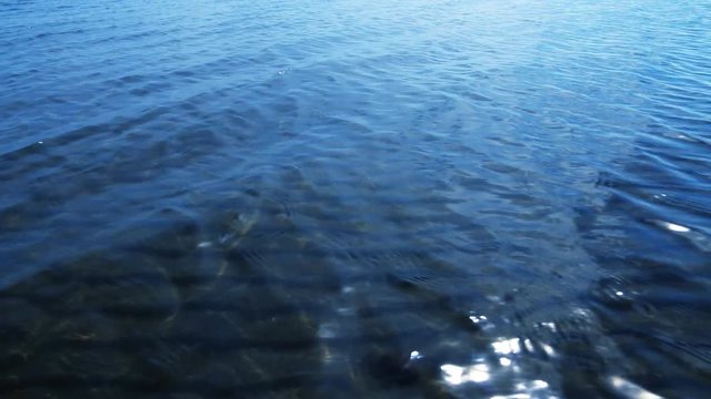 Deep blue sea with small wavelets sunlit and sandy seabed viewed through transparent water
