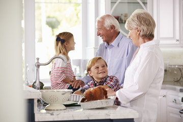 Obraz premium Children And Grandparents Make Roast Turkey Meal In Kitchen