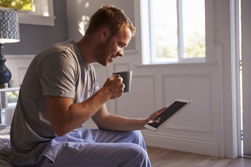 Man Wearing Pajamas Using Digital Tablet In Bedroom