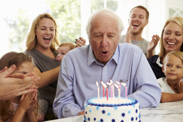 Grandfather Blows Out Birthday Cake Candles At Family Party