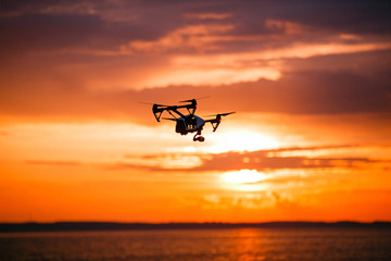 Naklejka na ściany i meble quadrocopter drone with remote control. Dark silhouette against colorfull sunset. Soft focus. Toned image