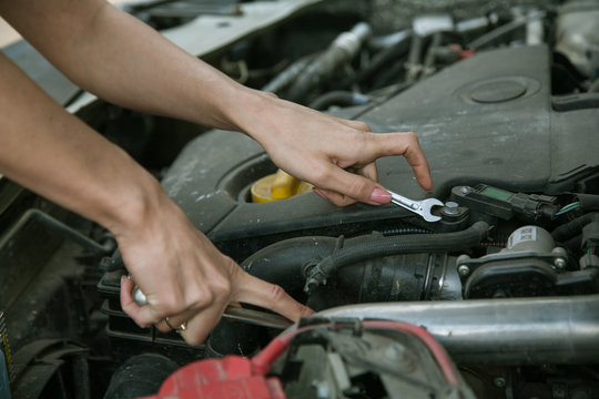 female hand with a wrench under the hood of the car