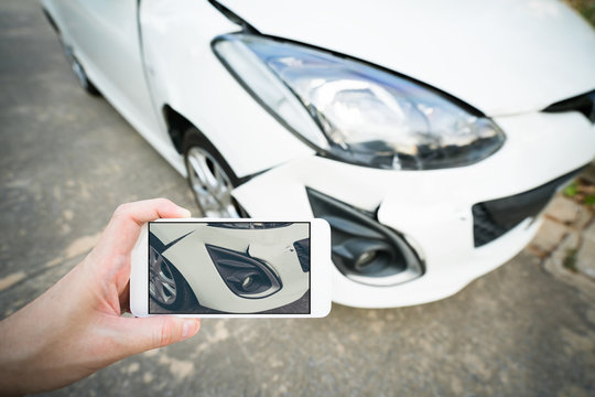 Man taking photo of damaged white car with smartphone
