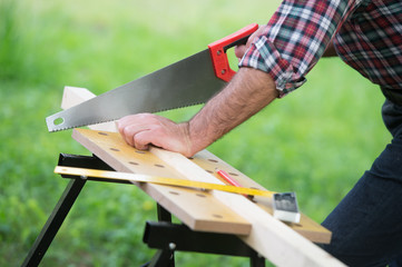 Carpenter sawing a wooden square with a wood saw