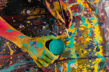 Hand hold paint bottle. Hands in paint. Woman painter. Colorful background.