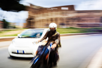 Fast scooter overtaking a car in a Roman street, with Coliseum in the background.
