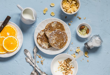 Breakfast table. Whole wheat pancakes, greek yogurt with homemade granola, orange slices, nuts, corn flakes, on a blue stone background