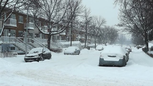 Residential street during a snowstorm. The cars are  covered in snow.