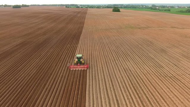 Aerial view of ploughed field with tractor sowing seeds of wheat. Industrial background on agricultural theme.Farm tractor and seeder planting crops on a field.Farm tractor handles field.