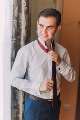 Young handsome looking man dressing up modern tie in hotel room