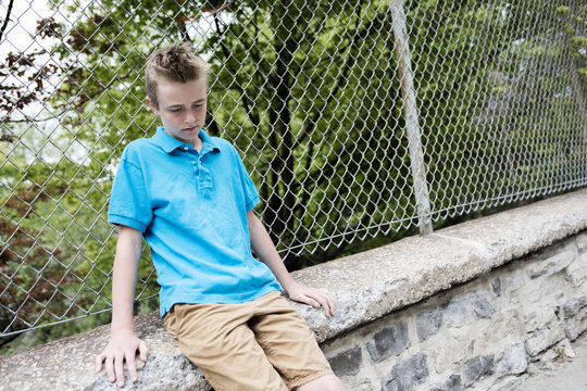 young teen boy looking out of a fence