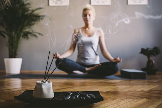 Woman practicing yoga in the gym with incense sticks in foreground