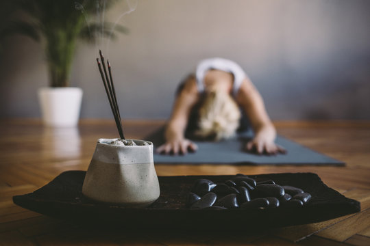 Woman practicing yoga in the gym with incense sticks in foreground