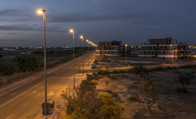 A half built Spanish apartment building, at night, with street lights illuminated along the road