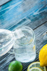 Glass jar and melted ice cubes with citrus fruits on a rustic wooden board