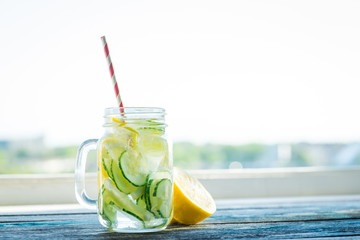 Jug with lemon and cucumber infused water on a rustic wooden surface