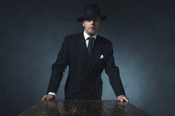Bossy vintage 1940 businessman standing behind wooden table.