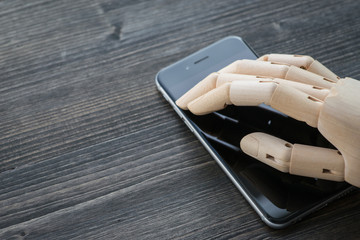 Artificial wooden hand with modern phone on wooden board