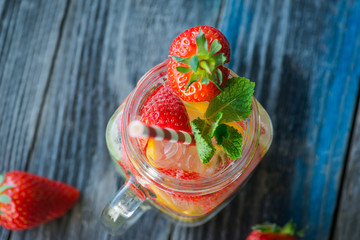 Jug with lemon and strawberry infused water on a rustic wooden surface