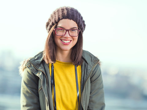 Portrait of beautiful smiling young woman wearing eyeglasses and hat walking in the city