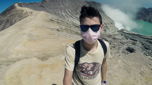 Teenager in dust mask taking selfie photo, video by Ijen volcano in Java, Indonesia
