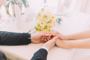 Close up male and female holding hands over white table with floral bouquet on it
