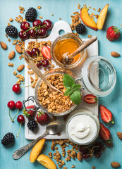Healthy breakfast ingredients. Oat granola in open glass jar, yogurt, fruit, berries, honey and...
