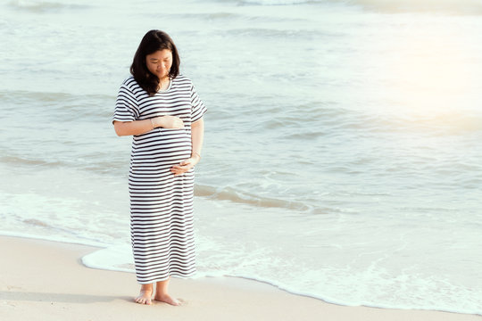 Pregnant woman holding her belly on the beach with copy space in vintage tone.