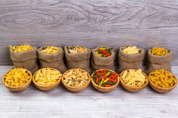 Various combinations of pasta on wooden background, burlap bags, bamboo bowls. diet and nutritional concept.