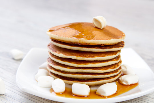 Tasty pancake on a white plate, wooden background, maple syrup