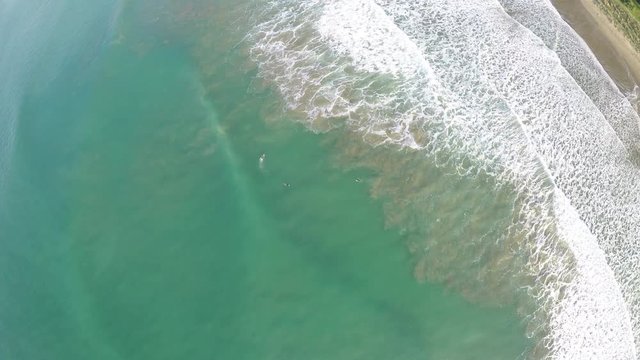 Birds eye aerial view of surfers riding waves at beach in Gisborne, New Zealand
