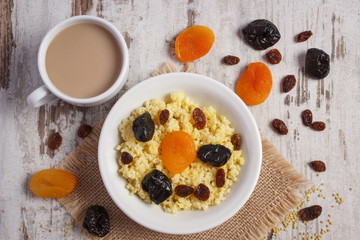 Cooked millet groats on white plate and cup of coffee with milk, healthy food and nutrition