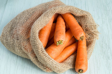 Carrot.   A sack with carrots on a light wooden background.