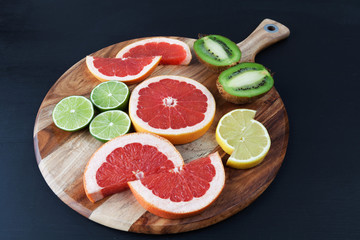 Slices of red grapefruit, lemon, kiwi, and lime on acacia chopping board. Horizontal image with copy space