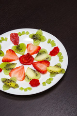 Sliced kiwi and strawberries lying in neatly placed pattern on white plate, as senn from above