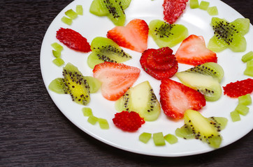 Sliced kiwi and strawberries lying in neatly placed pattern on white plate, as senn from above