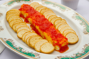 Thin crunchy toasted baguette slices stacked up on white plate with red salsa and cheese lying in middle