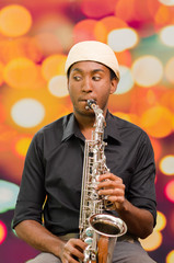 Fototapeta na wymiar African man wearing sixpence hat and dark shirt playing saxophone, facing camera
