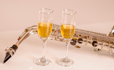Shiny saxophone lying on white surface, musical notes paper and two glasses of champagne sitting next to it