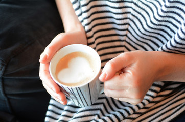Woman holds a mug with coffee in a shape of a heart