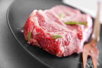 Raw pork steak with meat fork and rosemary on black plate