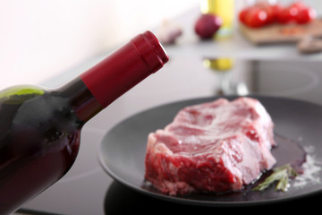 Raw pork steak with bottle of red wine on black plate