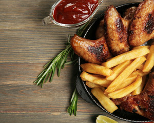 Baked chicken wings with French fries on wooden table