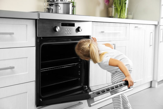 Little girl playing with oven in kitchen