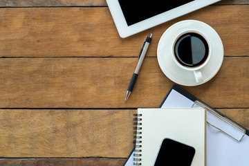 Office workspace with blank screen tablet, cup of coffee, pen, notebook, smartphone and paper over blackboard. Top view with copy space