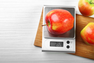Apple with digital kitchen scales on wooden background