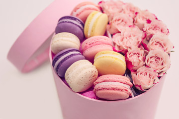 Tasty macaroons and roses in box on light background
