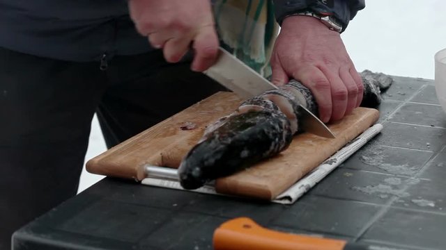 Cooking fish on a wood stove. The man is cutting a raw fish on a wooden board.
