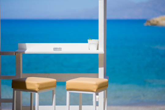 Bar stools at the beach bar close to the sea in the bay of Matala in the south-central of Crete. Famous by the caves is Matala also known as a hippie destination from the seventies - Powered by Adobe