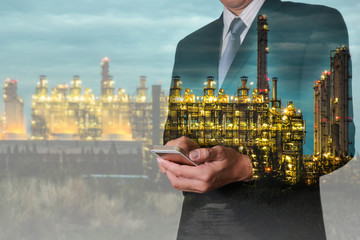 Double exposure of business man hand hold smart phone, mobile  and oil refinery industry plant, Electric Generating Factory in the night as communication of energy concept.